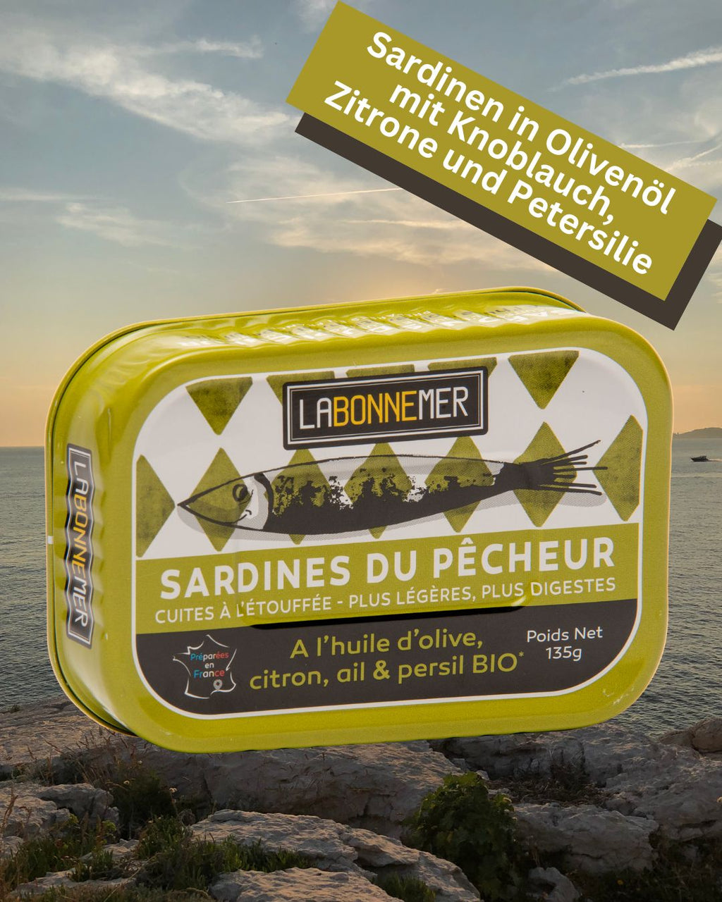 Grüne Dose der La Bonne Mer Sardinen BIO „Sardines du Pêcheur“ mit BIO-Zitrone, Knoblauch und Petersilie vor einer Küstenlandschaft im Sonnenuntergang bei Feinkost Mannheim. Sardinen online kaufen.