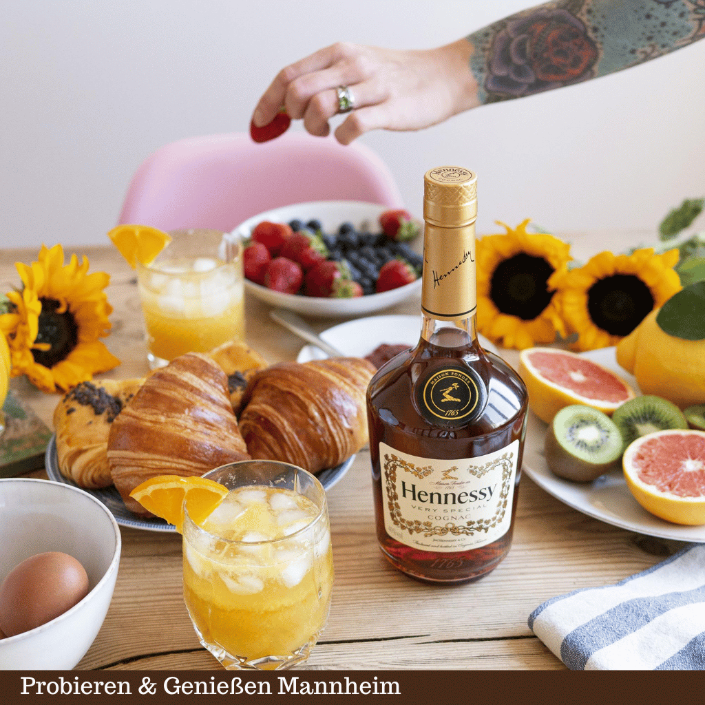 Eine Flasche Cognac Hennessy VS auf dem Tisch mit Obst, Croissant und Cocktail