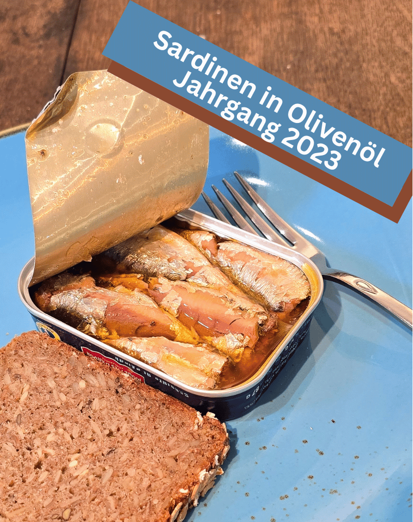 Eine offene Dose Jahrgangssardinen 2023 in Olivenöl – geöffnet, besonders aromatisch und zart im Geschmack. Blauer Teller mit Sardinendose und Brot. Feinkost online Mannheim