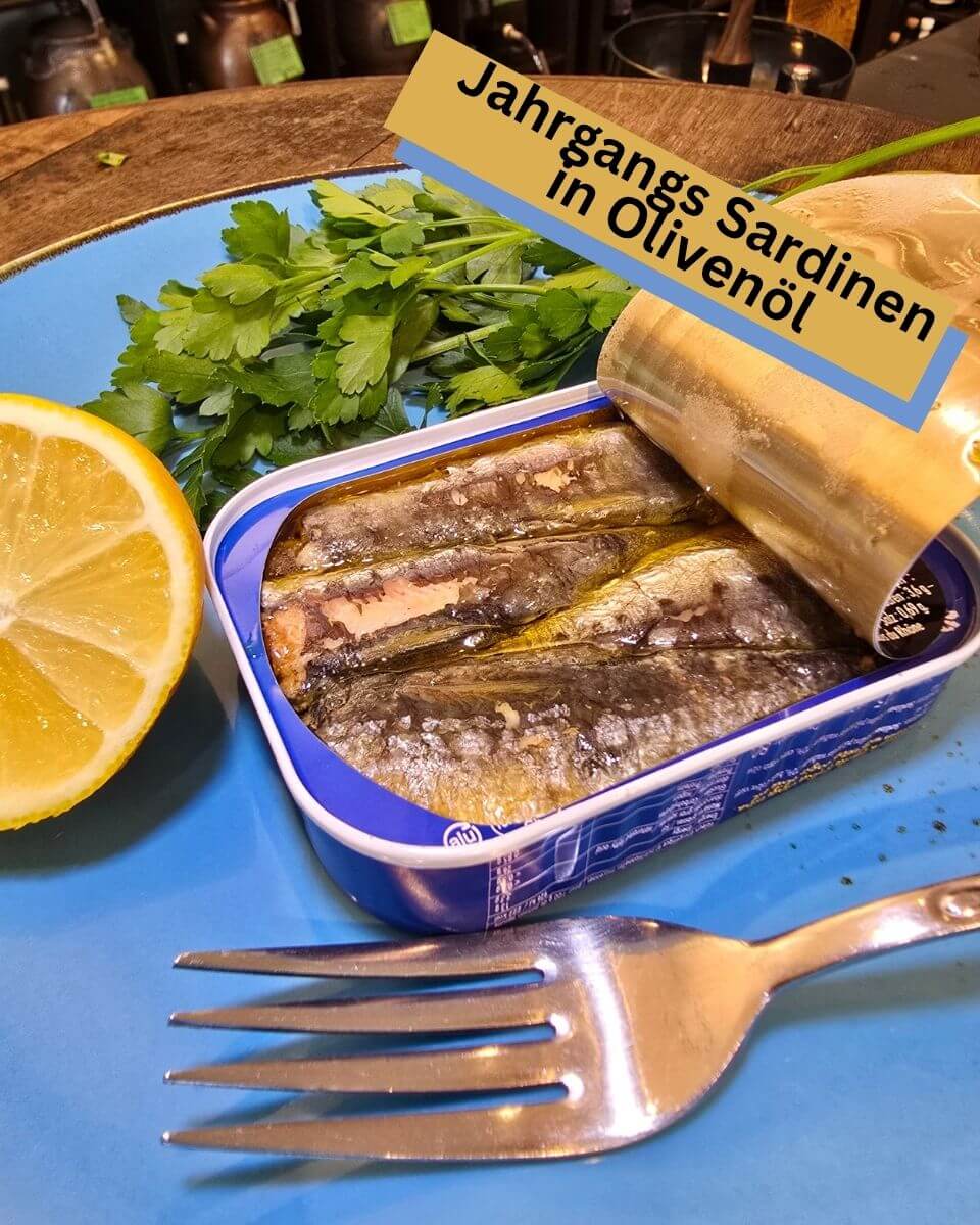 Jahrgangssardinen in Olivenöl in Mannheim. Geöffnete Dose auf blauem Teller serviert, zart und voller mediterraner Aromen mit Zitrone und Petersilie.