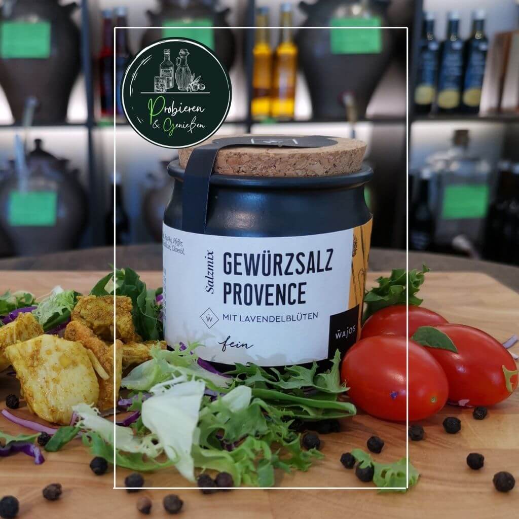 Provence Gewürzsalz mit Lavendelblüten in dekorativem Glasbehälter auf einem Holzbrett mit frischem Gemüse.