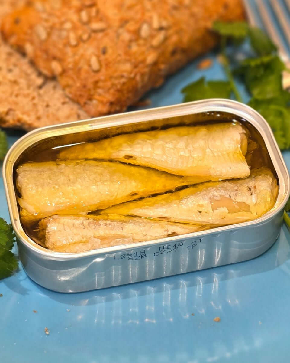 Eine geöffnete helle Dose mit Sardinen in Bio Olivenöl von Cantara Portugal auf einem blauen Teller mit Brot un Koriander in Mannheim