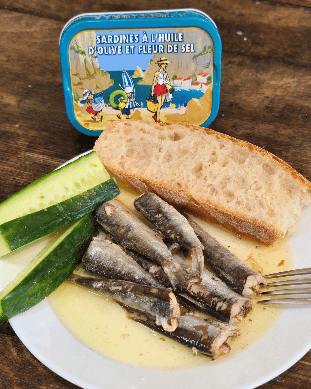 Ein weißer Teller mit LaBonneMer Sardinen in Olivenöl und Fleur de Sel mit Brot und grüner Gurke. Fisch Feinkost in Mannheim Innenstadt.