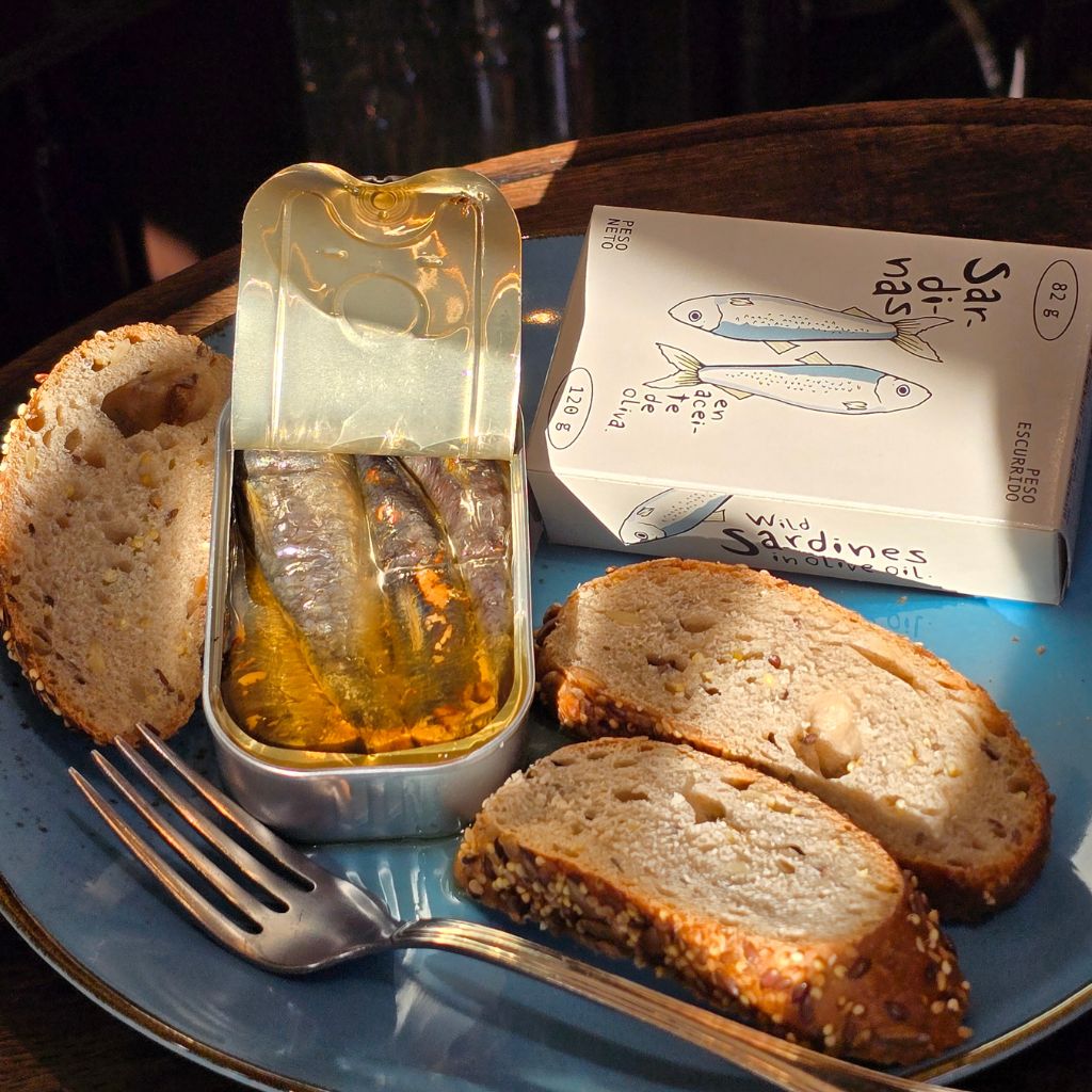 Geöffnete El Raño Sardinen in Olivenöl aus Spanien, serviert auf einem blauen Teller mit rustikalem Körnerbrot und Gabel bei Feinkost Probieren & Genießen in Mannheim.