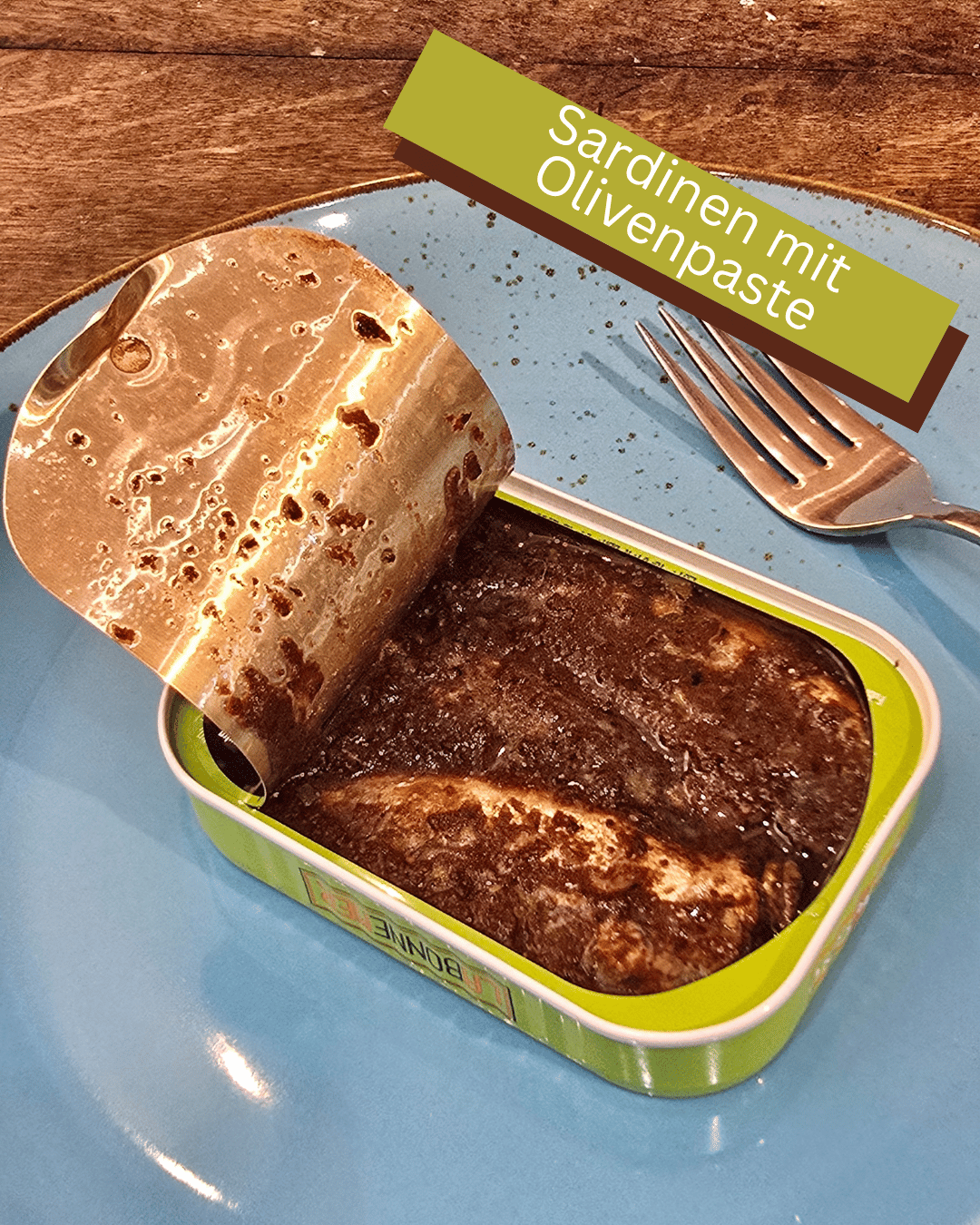 Geöffnete Dose La Bonne Mer Sardinen in Tapenade auf blauem Teller. Silbrig glänzende Sardinen in brauner Olivenpaste (Tapenade), französische Premium Fischkonserve in Mannheim